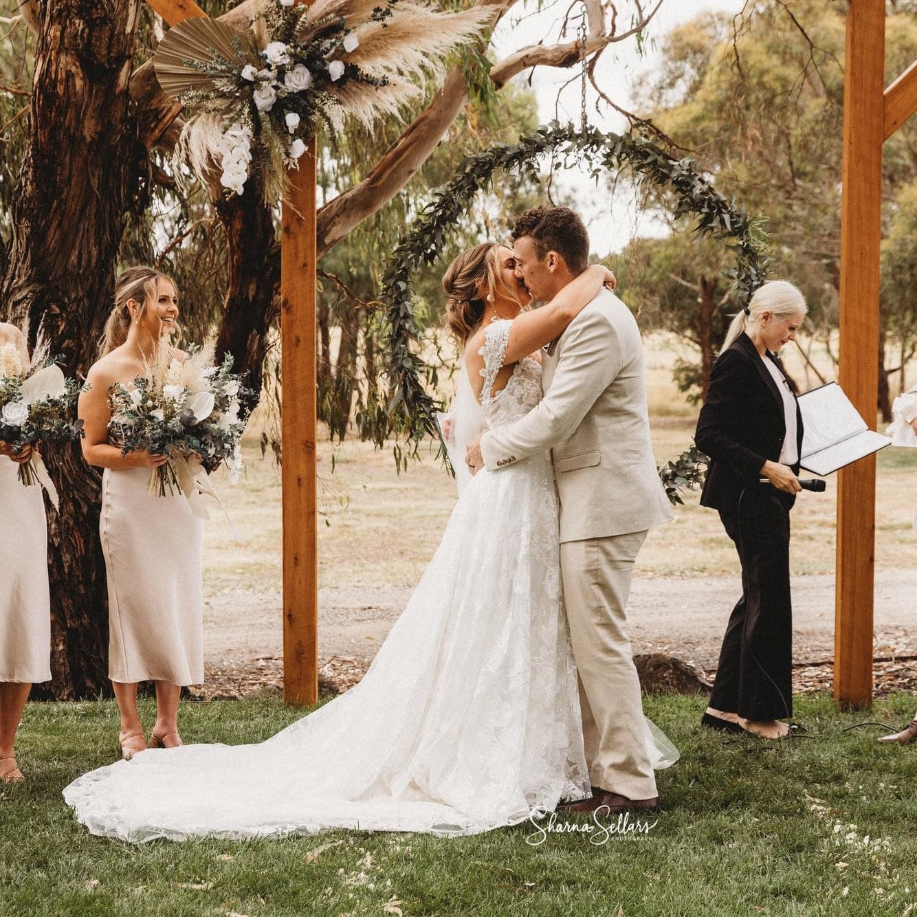 Ballarat wedding ceremony with floral backdrop hired from Bloomy Days. Bride and groom are kissing with wedding party watching.