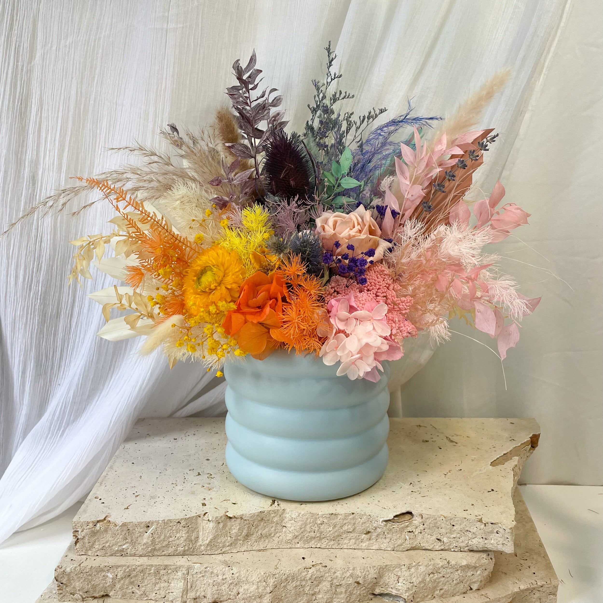 brightly coloured dried flower arrangement with light blue cylinder vase